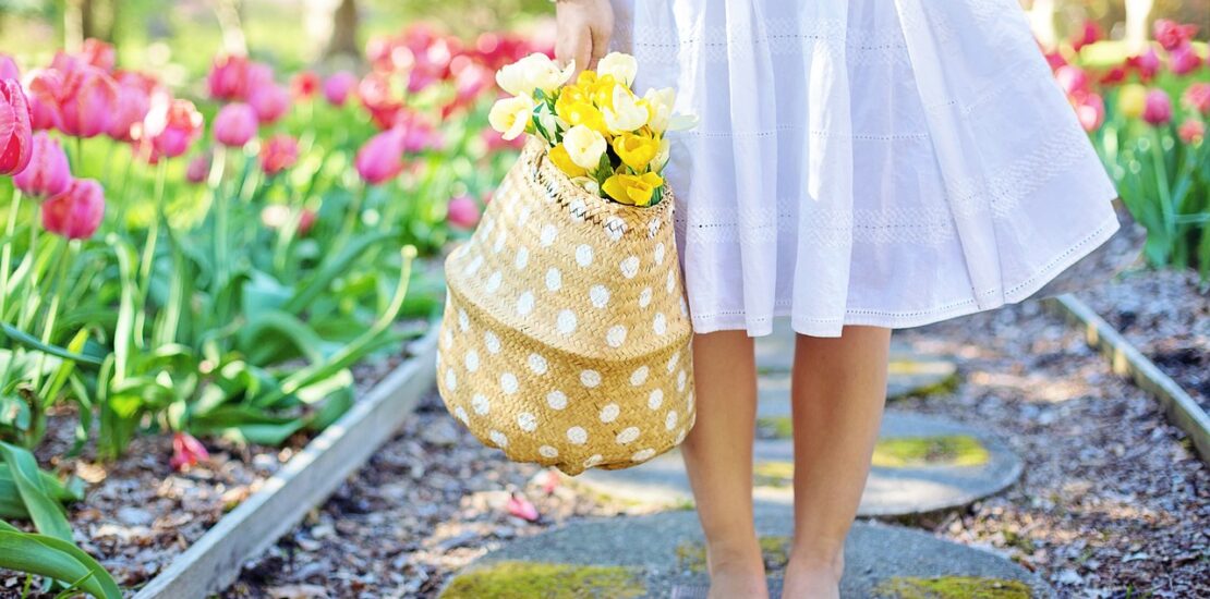 Girl carrying a flower basket, walking thorough a walkway with plant growth on each side. Blog Poster for "6 Creative Small Garden Ideas: Plantation & Design Guide"