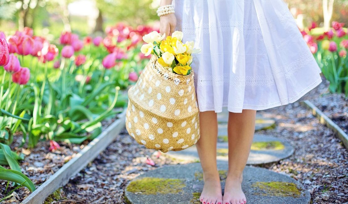 Girl carrying a flower basket, walking thorough a walkway with plant growth on each side. Blog Poster for "6 Creative Small Garden Ideas: Plantation & Design Guide"